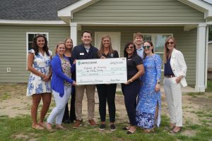A group of nine people, dressed in business casual attire, stand in front of a newly built light green house. In the center, two individuals from United Bank hold a large novelty check for $10,000 made out to "Habitat for Humanity of Horry County" for their "Financial Literacy Partnership." The check is dated July 30, 2025. The group appears happy and engaged, representing both organizations in a collaborative event. The foreground shows some grass and dirt, indicating a recently completed construction.