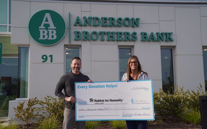 Male and Female standing in front of Anderson Brother Bank in Myrtle Beach holding a check for Habitat for Humanity of Horry County