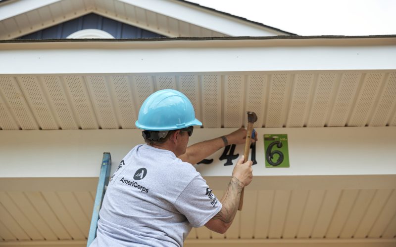 CHARLOTTE, NORTH CAROLINA, USA (06/28/2022) - AmeriCorps member nails house numbers on a new Habitat home on Faber Street in Charlotte, NC. Active Habitat AmeriCorps members and AmeriCorps alumni, who are now staff at Habitat for Humanity of the Charlotte Region, gather for a day of building. © Habitat for Humanity International/Carolina Guerrero.